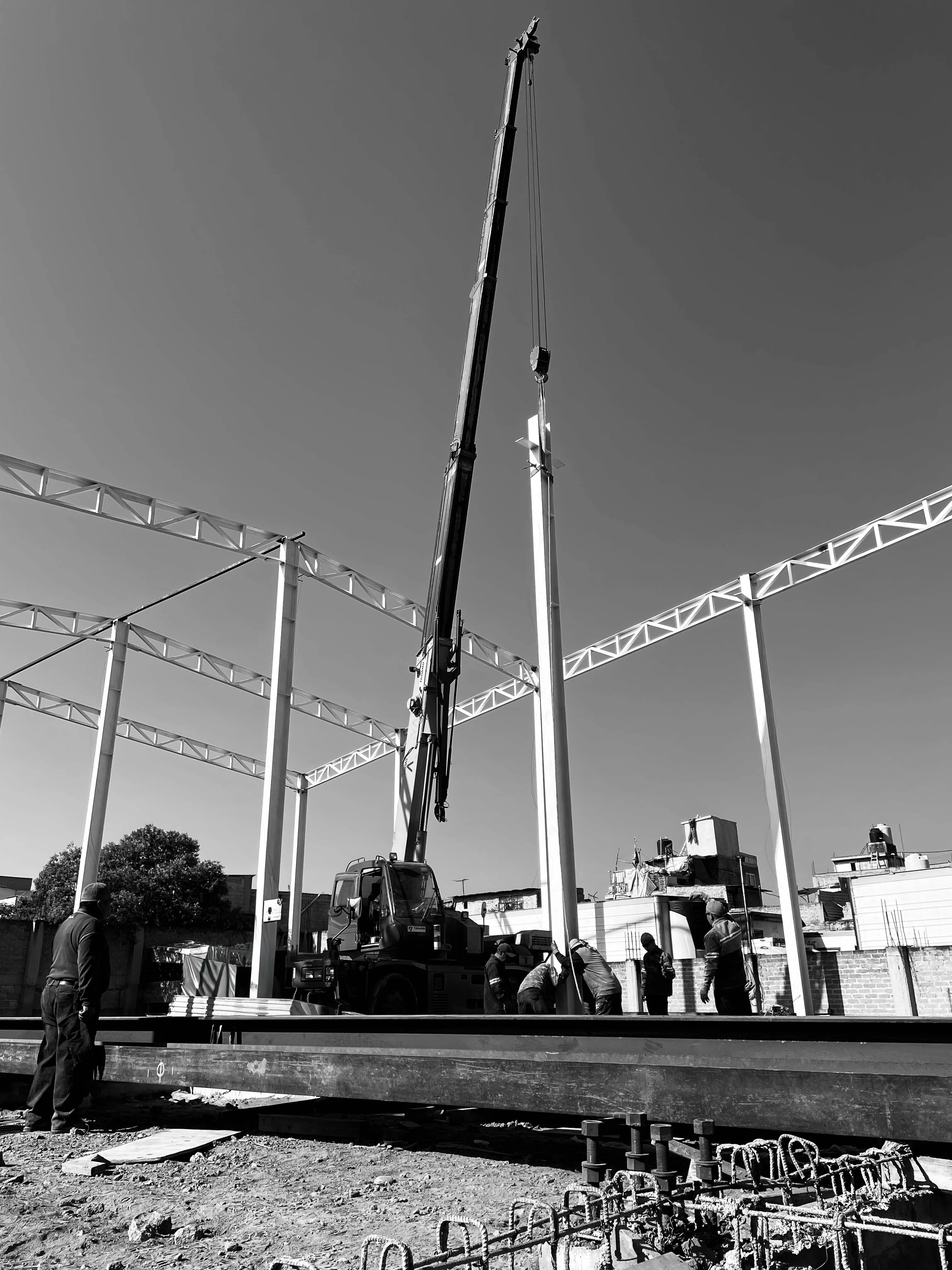 B&W: grúa montando columnas de acero contra cielo brillante.
